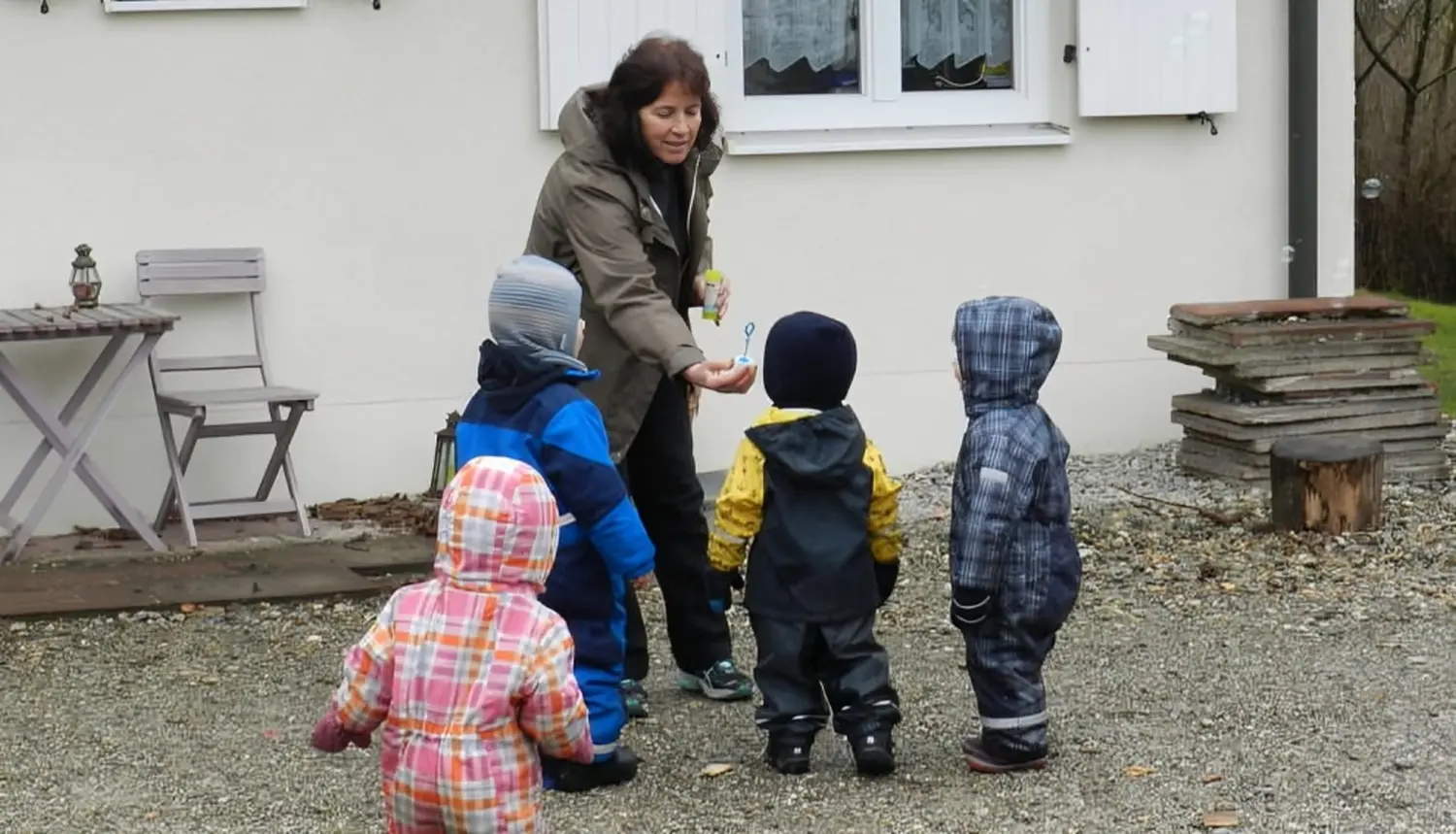Tagesmütter Augsburg-Land e.V. - Kita-Trägerverband - Eine erwachsene Frau überreicht vier kleinen Kindern in Wintermänteln im Freien ein Spielzeug.