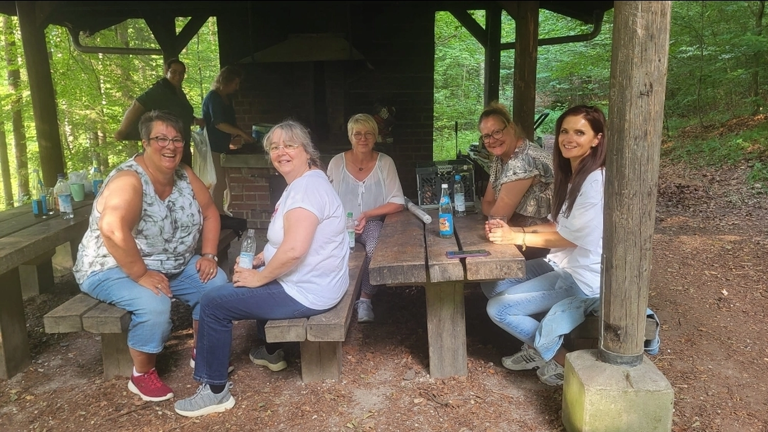 Tagesmütter Augsburg-Land e.V. - Kita-Trägerverband - Eine Gruppe von fünf Frauen sitzt um einen rustikalen Holzpicknicktisch unter einem Pavillon im Freien.